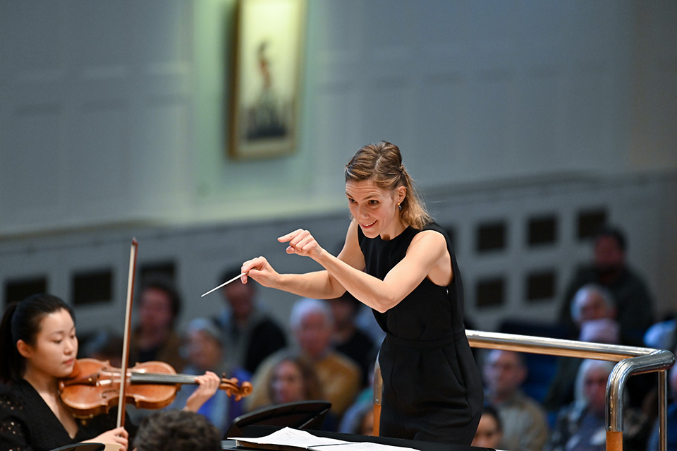 A woman dressed in black conducting an orchestra